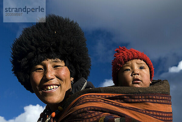 Eine Frau trägt in Thanza  Bhutan  ein Kind auf dem Rücken.