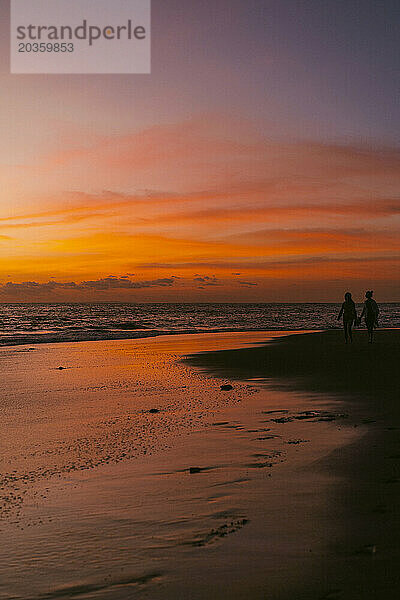 Menschen gehen bei Sonnenuntergang am Meer entlang.
