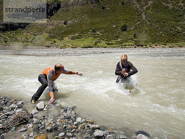 Zwei Männer überqueren auf einer Expedition in den chilenischen Anden einen Fluss.