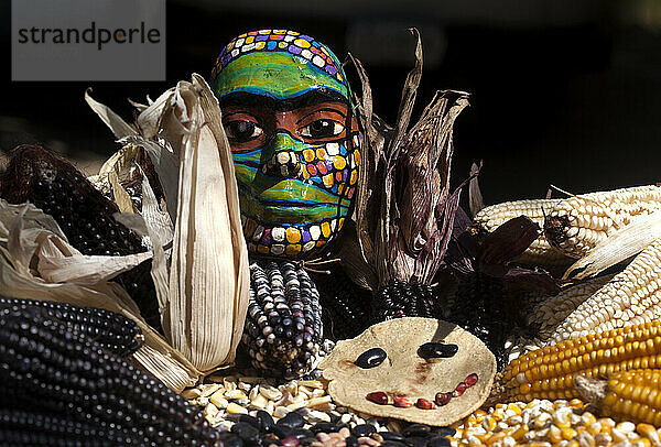 Eine farbige Maske schmückt einen Tisch voller Maiskolben in der „Tepetlixpa Seed Bank“  die von Tomas Villanueva Buendia „Tomaicito“ zum Schutz und zur Rettung der ursprünglichen Sorten Mexicas gegründet wurde