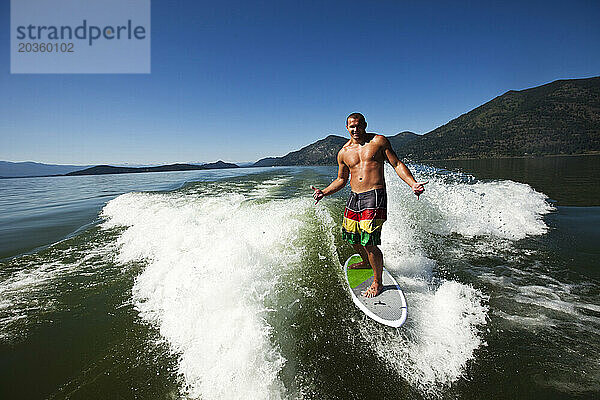 Ein glücklicher  sportlicher Mann lächelt beim Wakesurfen hinter einem Wakeboard-Boot in Idaho.