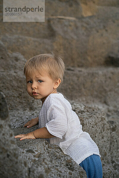 Porträt eines kleinen blonden Jungen auf einem Felsen. Bali.