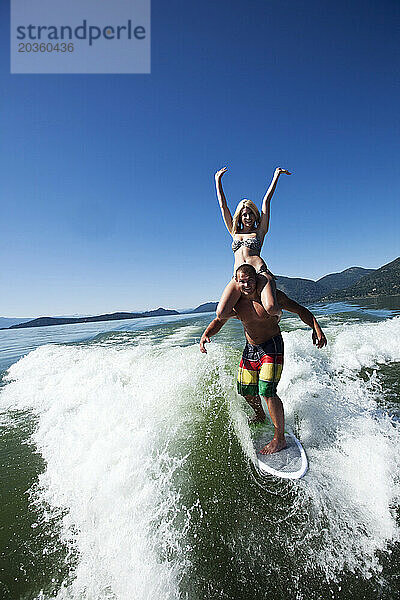 Ein glückliches Paar lacht und lächelt beim Wakesurfen mit dem Mädchen auf seinen Schultern hinter einem Wakeboard-Boot in Idaho.