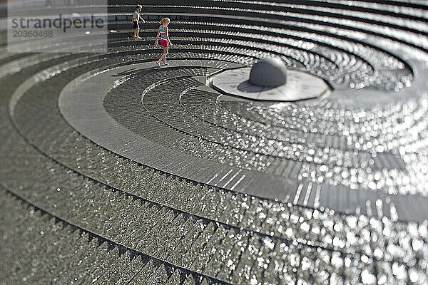 Ein kleiner Junge und ein Mädchen gehen um einen Brunnen im Freien am Darling Harbour in Sydney  New South Wales  Australien.