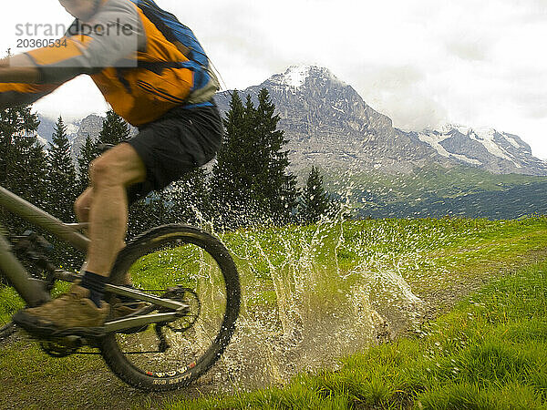 Ein Mountainbiker fährt durch ein Schlammloch auf dem Radweg Richtung First. Im Hintergrund der Eiger.