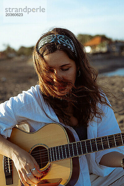 Musikerin singt und spielt Gitarre am Strand. In einem Bandana. Bali