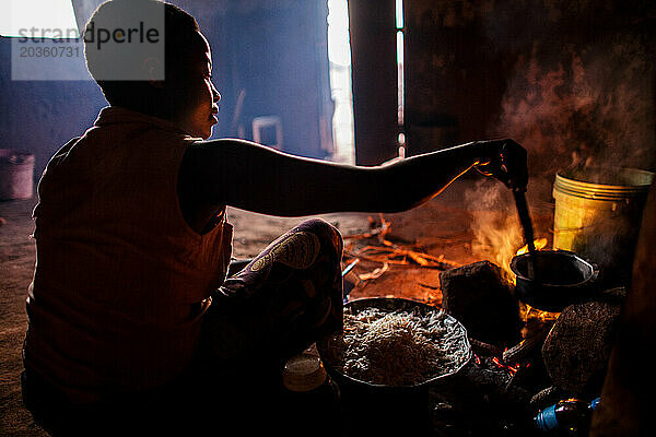 Tansanische Frau kocht Abendessen auf einem traditionellen Dreisteinofen