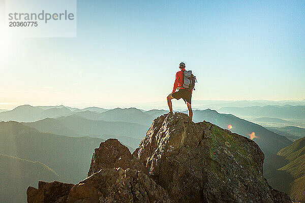 Erfolgreicher Mann steht bei Sonnenuntergang auf dem Berggipfel