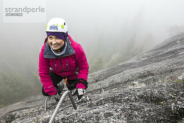 Eine Frau greift beim Klettern auf der Via Ferrata in Squamish  British Columbia  nach der Metallsprosse.