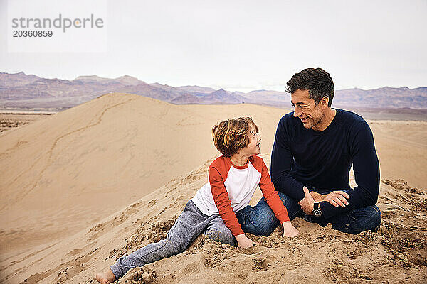 Vater und Sohn haben Spaß  während sie auf einer Sanddüne im Death Valley sitzen