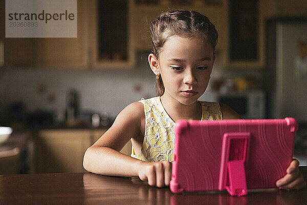 Mädchen sitzt mit einem Tablet am Tisch