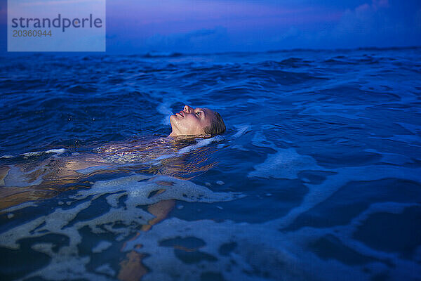 Eine Frau im Bikini schwimmt in der Abenddämmerung im Meer.