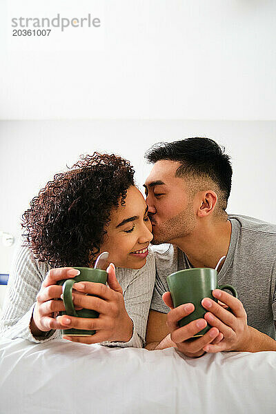 Multiethnisches glückliches Paar küsst sich liebevoll im Bett.