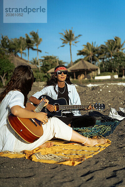 Musikerin singt und spielt Gitarre am Strand. In einem Bandana. Bali