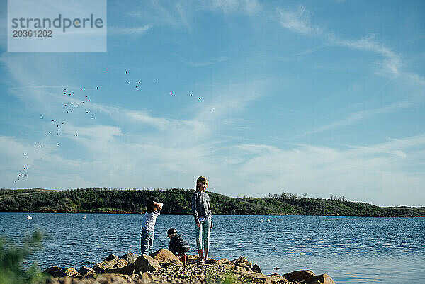 Weitblick auf drei Kinder  die am felsigen Ufer des Sees spielen.