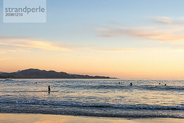 Surfer genießen bei Sonnenuntergang ruhige Wellen.