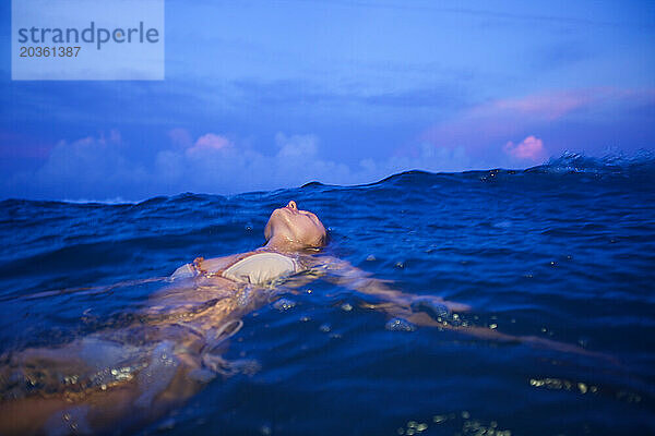 Eine Frau im Bikini schwimmt in der Abenddämmerung im Meer.