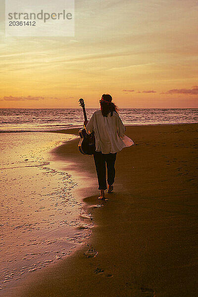 Musikerin mit Gitarre am Strand bei Sonnenuntergang. Bali