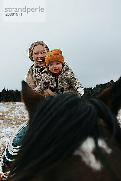 Mutter hält ihr Baby auf dem Pferd und genießt den fröhlichen Ritt