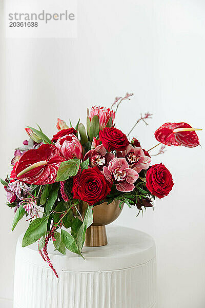 Lebendiges Blumenarrangement in großen Rottönen in einer goldenen Vase