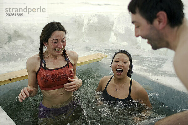 Drei Personen in einem Pool im zugefrorenen Baikalsee im Winter auf der Insel Olchon  Sibirien  Russland.