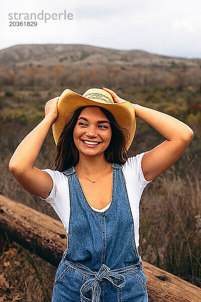 Junge Frau hält Hut und lächelt in die Ferne