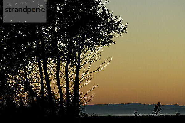 Eine Frau radelt bei Sonnenuntergang am Iona Beach  Richmond  British Columbia  Kanada. (Silhouette)