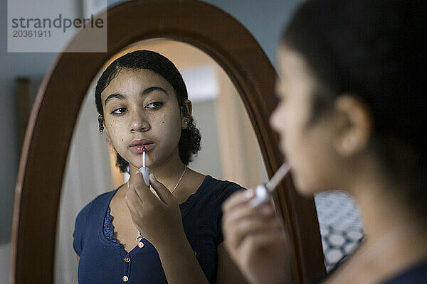 Biracial Teen Girl trägt im Spiegel Lipgloss auf