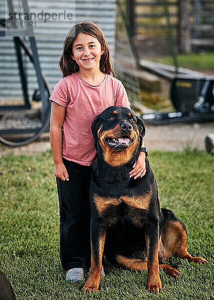 Porträt eines lächelnden Mädchens  das mit dem Arm um Rottweiler auf Gras steht