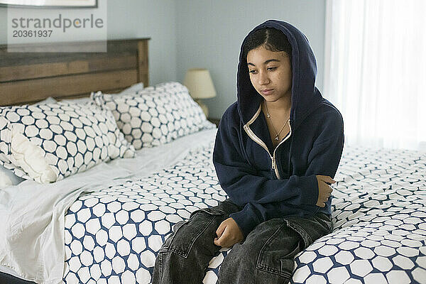 Ein gemischtrassiges Teenager-Mädchen sitzt auf dem Bett und sieht deprimiert aus