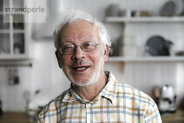 Porträt eines älteren  fröhlichen Mannes  der in einer gemütlichen Küche steht und lächelt