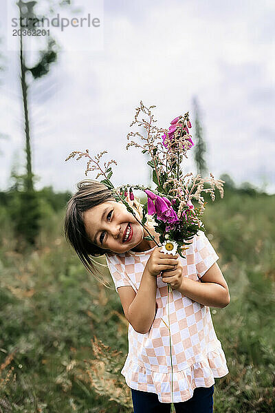 Asiatisches Mädchen lächelt mit Blumen  während die Sonne auf dem Feld scheint