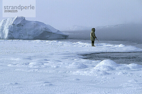 Eine vermummte Person hält ein Gewehr und steht inmitten von Schnee  Nunavut  Kanada.