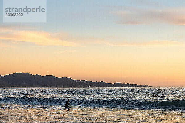 Surfer genießen kleine Wellen bei Sonnenuntergang.