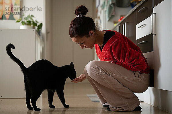 Frau füttert schwarze Katze mit der Hand in der Küche