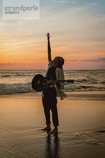 Musikerin mit Gitarre am Strand bei Sonnenuntergang. Bali