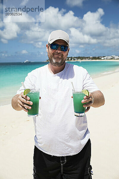 Glücklicher bärtiger Mann hält zwei tropische Getränke am karibischen Strand