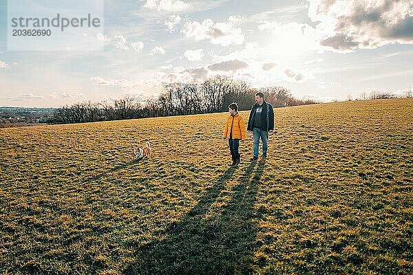 Ein Junge  sein Vater und ein Corgi laufen an einem sonnigen Tag durch ein Feld