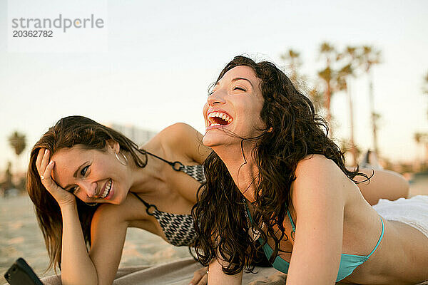 Zwei Frauen lachen  während sie den Nachmittag am Strand verbringen.