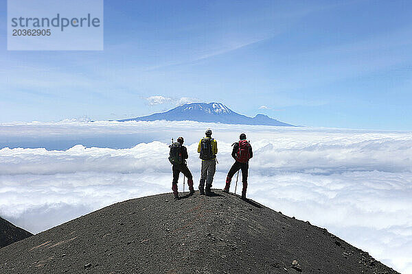 Drei Wanderer blicken vom felsigen Grat des Mount Meru auf den Kilimandscharo.