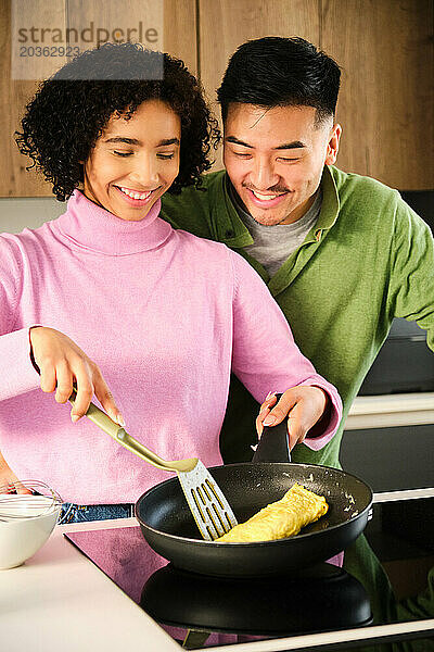 Multiethnisches Paar kocht gemeinsam Omelette in der Küche.