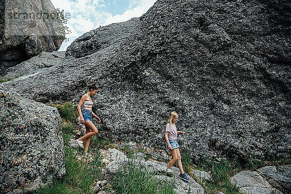 Seitenansicht von zwei Teenager-Mädchen  die im Sommer Felsen hinunterwandern.