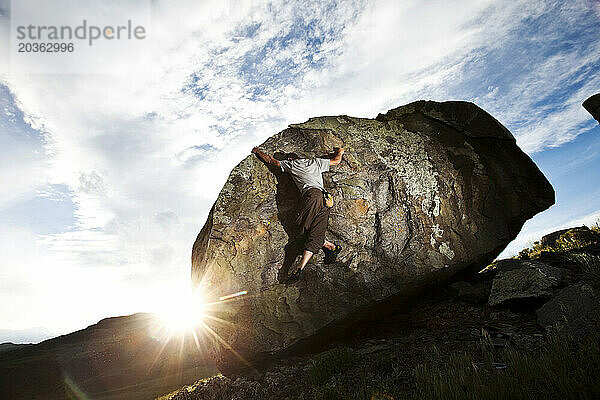 Ein sportlicher junger Mann arbeitet bei Sonnenuntergang in Montana an einem Boulderproblem.