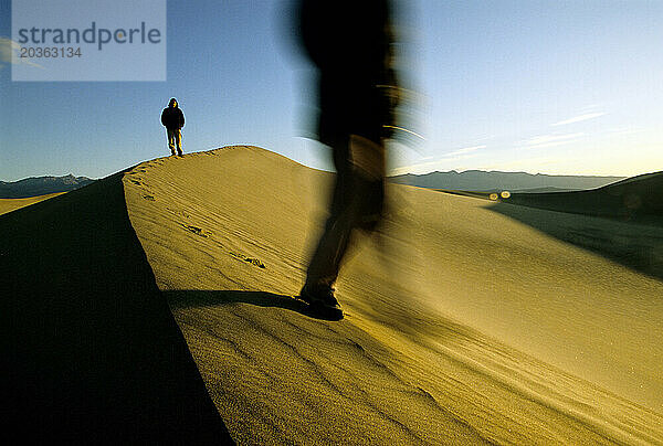 Zwei Menschen gehen bei Sonnenaufgang durch eine Wüste  Death Valley  Kalifornien.