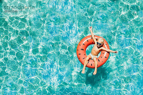 Drohnen-Luftaufnahme eines glücklichen Jungen im Pool im Sommer mit Wassermelonen-Float