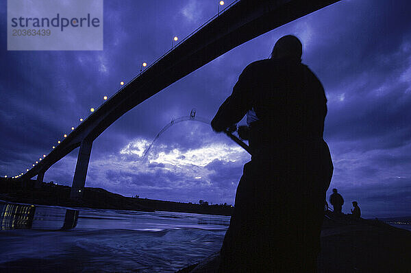 Eine Silhouette einiger Männer  die unter einer Brücke fischen.