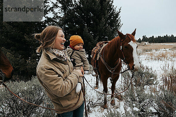 Lächelnde Mutter und Baby  die freudig Pferde draußen halten