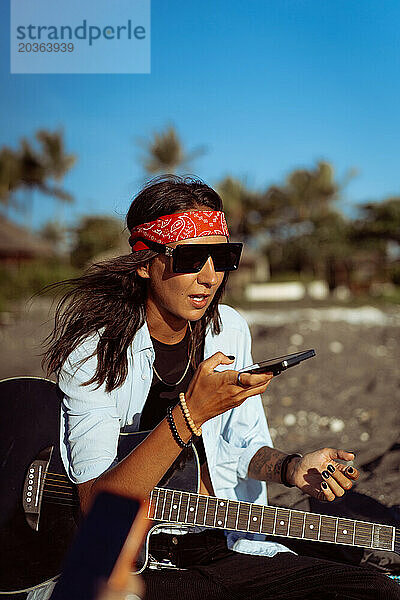 Musikerin singt und spielt Gitarre am Strand. In einem Bandana. Bali