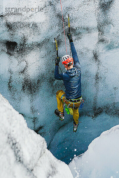 Ein Mann  der gerne draußen unterwegs ist  klettert eine Eiswand auf einem isländischen Gletscher hinauf