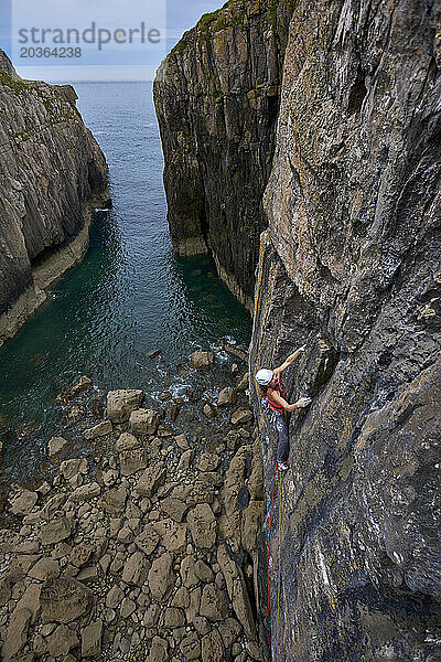 Seitenansicht einer abenteuerlustigen Frau  die eine Klippe an der Küste von Pembroke  Wales  Großbritannien  hinaufklettert